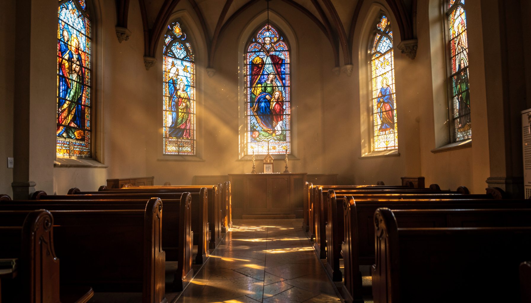 Sunlight streaming through stained glass windows in a quiet church sanctuary, casting warm amber and deep blue hues across wooden pews.